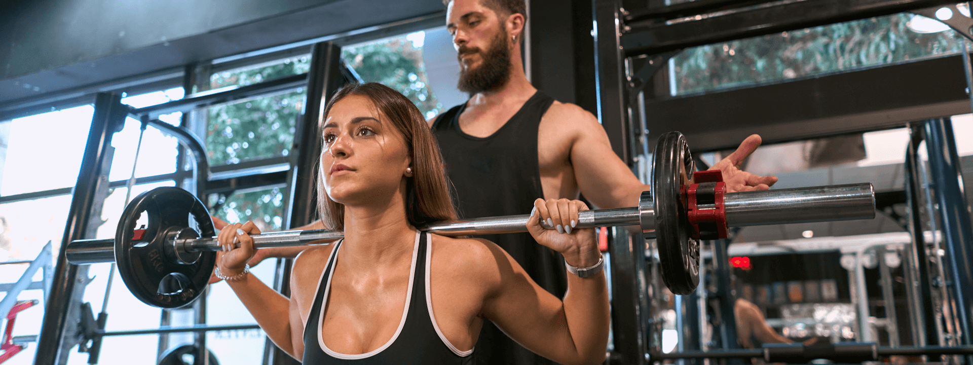 Coach sichert junge Frau bei Kniebeugen